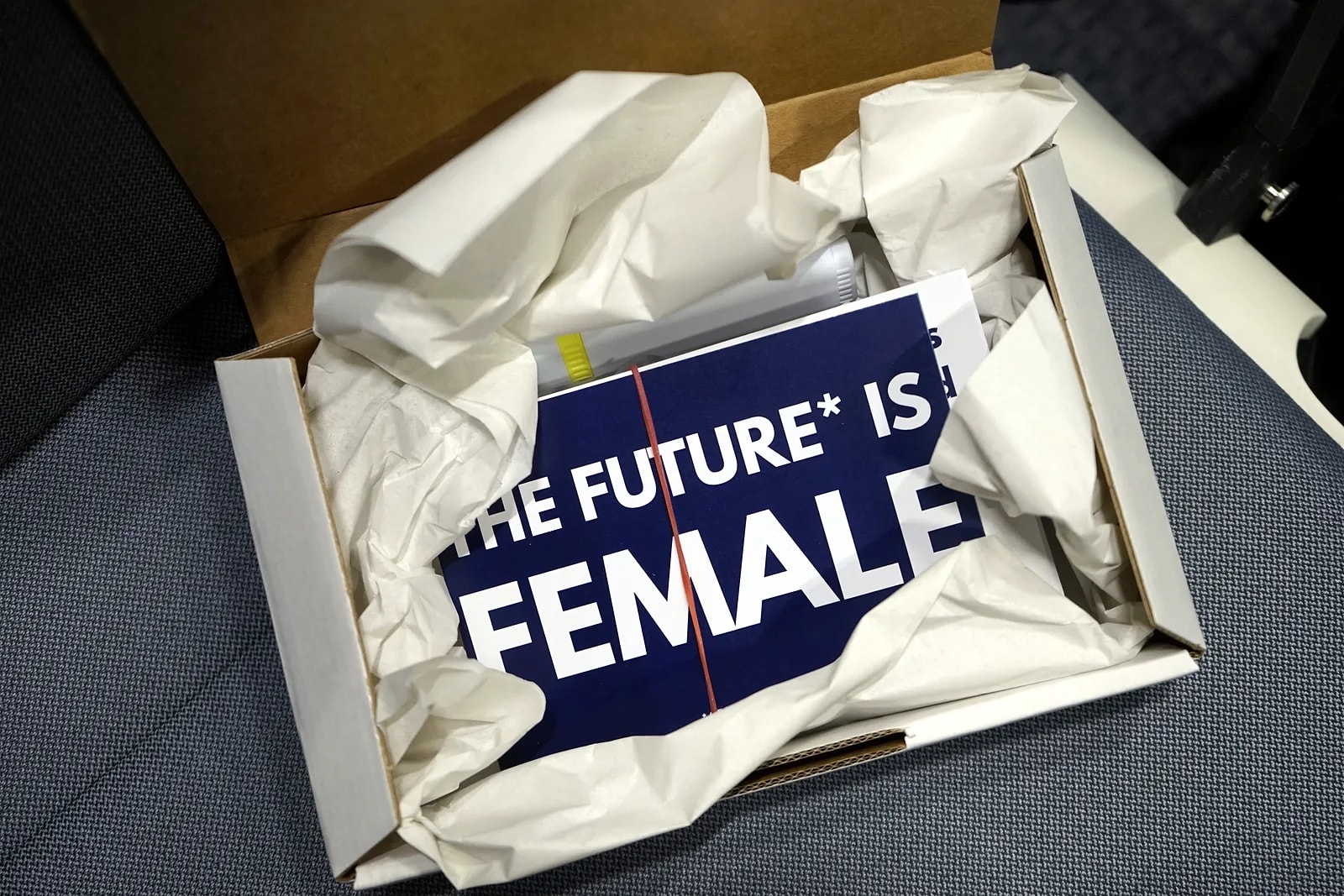 Ein geöffnetes Willkommenspaket, darin ein Druck mit der Aufschrift „THE FUTURE* IS FEMALE“.
